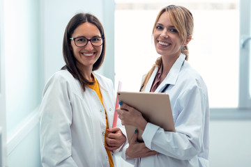 Two beautiful young female doctor holding digital tablet while smiling looking at camera in hospital.