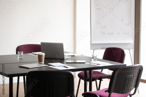 Time-out in strategy planning. Empty boardroom with conference table and comfortable chairs prepared for briefing, flip chart with infographics and laptop. Workplace for business team, office for rent
