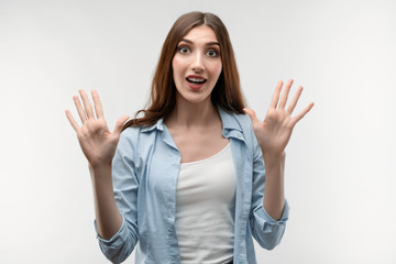 Studio shot of surprised Young female with long chestnut hair smiling happily and raises her hands. Surprise