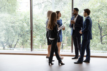 Group Of Multiethnic Managers Or Employees Standing In Modern Office Hall After Staff Briefing And Discussing Corporate News, Diverse Business Teammates Gather Together To Share Information And Plans