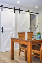 Selective Focus On A Bright Dining Room With A Wooden Table And Rattan Chairs. White Sliding Barn Doors In The Background.