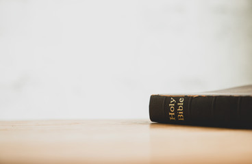 Holy bible with note book and pencil on wooden table against morning sun light for christian devotion, copy space
