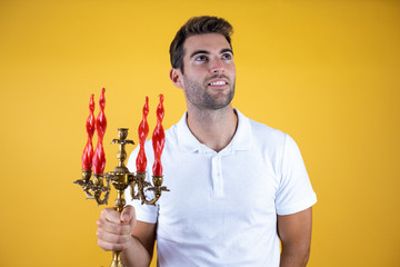 handsome man over insolated yellow background holding a chandelier with red candles.