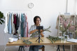 © fizkes - Smiling attractive young female professional decorator blogger sitting at table in front of mobile phone on stabilizer, filming educational diy bouquet video, recording online workshop in office.