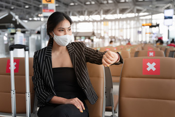 young woman with flu mask checking time to on boarding in departure area.