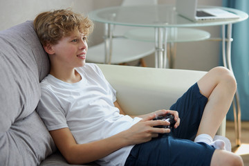 young caucasian redhead boy playing video games alone at home, leisure time concept