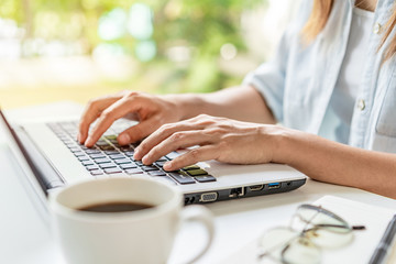 Wall Mural - Young woman with cup of coffee sitting at living room and working on laptop at home