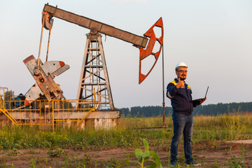 engineer with a laptop on the background of an oil pump