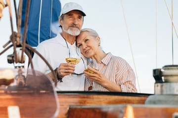 Wall Mural - Mature couple standing on a private yacht and drinking wine. Two senior people enjoy sailing and each other.