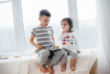 Brother and sister are sitting on the windowsill and reading a book. Happiness, family