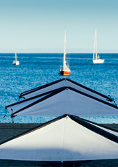 Sticker - Vertical shot of tents at the beach with boats sailing in the background