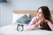 © BestForYou - Smiling young woman lying awake in bed with alarm clock, good morning.