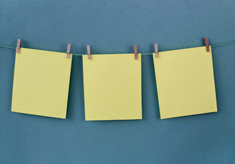 Three yellow blank sheets of paper hang from a rope against a blue background. Note paper. Reminder. Place for your text.
