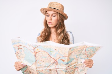 Young caucasian woman with blond hair wearing summer hat holding map relaxed with serious expression on face. simple and natural looking at the camera.