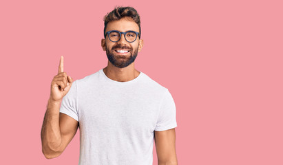 Young hispanic man wearing casual clothes and glasses showing and pointing up with finger number one while smiling confident and happy.