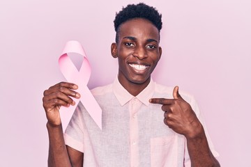 Young african american man holding pink cancer ribbon pointing finger to one self smiling happy and proud