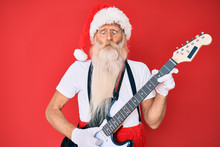 Old Senior Man Wearing Santa Claus Costume Playing Electric Guitar Making Fish Face With Mouth And Squinting Eyes, Crazy And Comical.