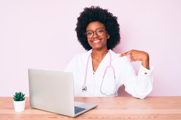 Young african american woman wearing doctor stethoscope working using computer laptop pointing finger to one self smiling happy and proud