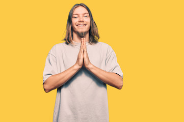 Wall Mural - Handsome caucasian man with long hair wearing casual clothes praying with hands together asking for forgiveness smiling confident.