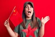 Beautiful patriotic woman wearing t-shirt with red star communist symbol holding china flag celebrating achievement with happy smile and winner expression with raised hand