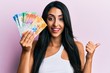 © Krakenimages.com - Beautiful hispanic woman holding swiss franc banknotes pointing thumb up to the side smiling happy with open mouth