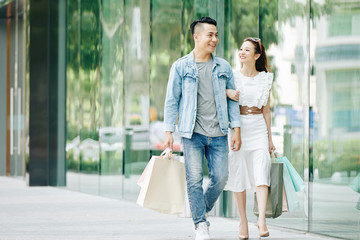 Canvas Print - Happy pretty young Asian woman looking on her boyfriend when they are walking outdoors after shopping