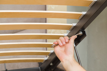 Young man hand using wrench and screwing screw in parts of metal steel for mattress bed. Assembling new furniture. Closeup.