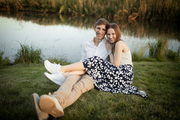 Wall Mural - The young couple is sitting on the grass. Happy married couple outside on nature