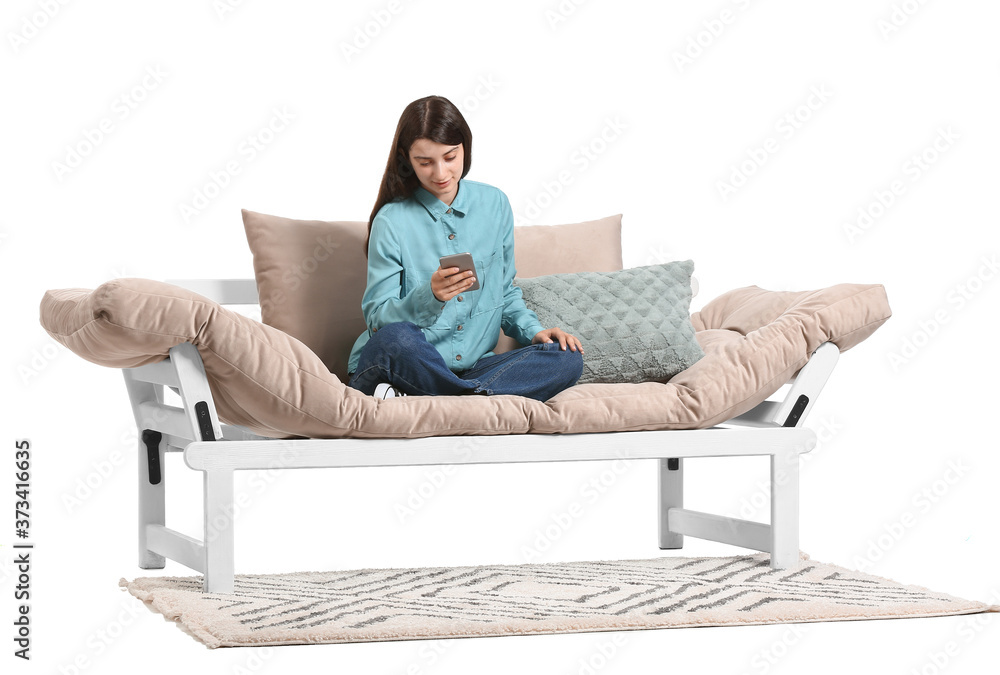 Young woman with mobile phone sitting on sofa against white background