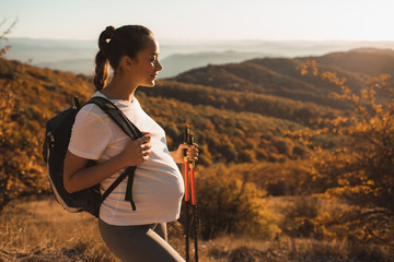pregnant woman nordic walking with trekking sticks on hill with beautiful autumn mountain view. preg
