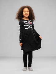 Wall Mural - halloween, holiday and childhood concept - smiling african american girl in black costume dress with skeleton bones over grey background