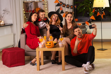 Wall Mural - friendship, holiday and people concept - group of happy smiling friends in halloween costumes of vampire, devil, witch and cheetah taking selfie by smartphone at home party at night