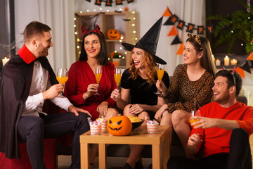 Wall Mural - friendship, holiday and people concept - group of happy smiling friends in halloween costumes of vampire, devil, witch and cheetah with non-alcoholic drinks at home party at night