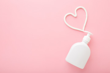 Wall Mural - Heart shape created from cream. White pump bottle on light pink table background. Pastel color. Care about face, hands, legs and body skin. Closeup. Empty place for text or logo. Top down view.