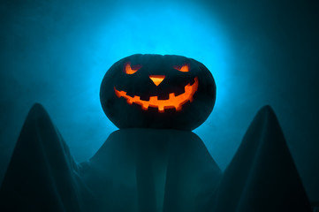 Halloween concept. A ghost with a creepy head glowing jack-o-lantern pumpkin stands in the fog at dusk.