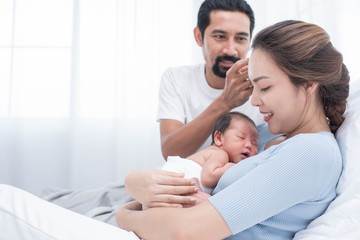 Wall Mural - smiling mother and father holding their newborn baby at home..portrait of happy family at home, young parents holding on hands little sweet newborn baby, love and happiness concept.