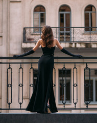 mysterious silhouette of an elegant retro woman. a lady in long black evening dress stands on the ba