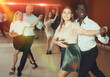 Portrait of positive adult pairs enjoying dancing salsa in modern dance studio