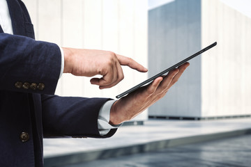 Man presses on the screen of a digital tablet near the exterior of the business center on a sunny day, close up. Online technology concept