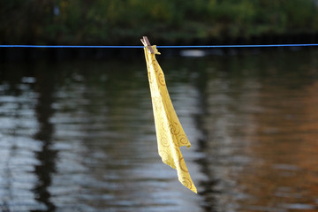 Wall Mural - Closeup shot of a yellow textile hanging on a rope with a clothespin against a blurry water