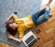 © olezzo - Beautiful young female in a yellow shirt lying on the floor on a carpet with a laptop, freelancer and home office concept. Top view shot image
