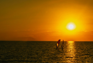 sunset at sea and two sail surfing sails on the horizon