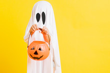 Funny Halloween Kid Concept, Little Cute Child With White Dressed Costume Halloween Ghost Scary He Holding Orange Pumpkin Ghost On Hand, Studio Shot Yellow On White Background