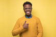 © Viktor Koldunov - Handsome black man in glasses shoing thumb up. Studio shot on yellow wall.