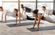 © Prostock-studio - Group of sporty people practicing yoga together, standing in plank phalankasana pose