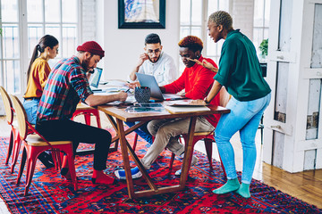 Wall Mural - African American teacher explaining difficult information to absorb during private lesson with small group of diverse students, creative coworkers collaborate on project report during exam preparation