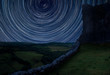 Digital composite image of star trails around Polaris with Ruined medieval castle landscape with dramatic sky