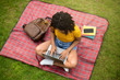 Above view of focused black lady using laptop computer on picnic blanket at park