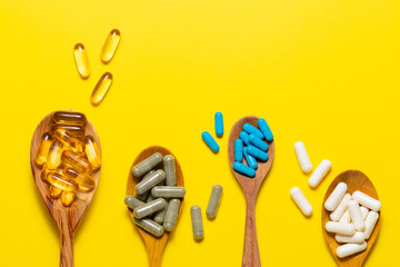 Wall Mural - Assortment on natural medical capsules for healthy lifestyle and beauty in the wooden spoons on yellow background top view. Health care concept. Immunity support mix.