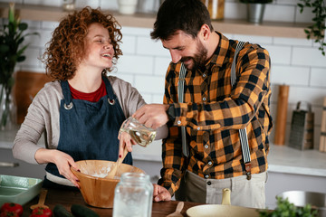 Wall Mural - Boyfriend and girlfriend making delicious food at home. Loving couple cooking in kitchen..